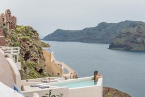 une femme assise au bord d'une piscine donnant sur l'océan dans l'établissement Art Maisons Oia Castle, à Oia