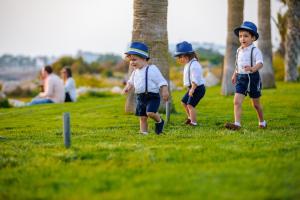 tre bambini che indossano cappelli che camminano nell'erba di Blue Lagoon Kosher Hotel (by Capital Coast Resort & Spa) a Paphos