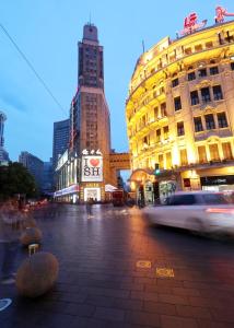 eine Stadtstraße mit Gebäuden und einem vorbeifahrenden Auto in der Unterkunft Seventh Heaven Hotel in Shanghai