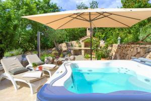 einen Pool mit einem Sonnenschirm und Stühlen sowie einem Whirlpool in der Unterkunft White Cottage Heritage House in Čižići