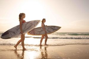 twee meisjes lopen op het strand met hun surfplanken bij Blue Heron Boutique Motel in Gold Coast