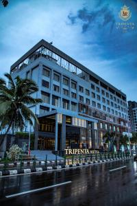 a tall white building with a palm tree in front of it at KPM TRIPENTA HOTEL in Kozhikode