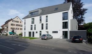 un bâtiment blanc avec deux voitures garées devant lui dans l'établissement Ferienwohnung Wilhelmstraße, à Tübingen