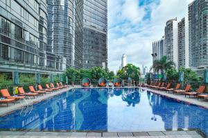 une grande piscine avec des chaises orangées et des bâtiments dans l'établissement Fraser Suites Guangzhou, à Canton