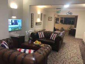 a living room with leather couches and a tv at Penny Farthing Hotel & Cottages in Lyndhurst