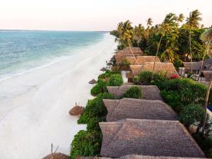 einen Strand mit einer Reihe von Strohschirmen und dem Meer in der Unterkunft Zanzibar Sunrise at Bandas in Matemwe