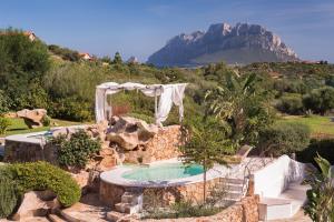 uma piscina num jardim com uma montanha ao fundo em Hotel Ollastu em Costa Corallina