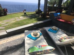 deux chapeaux assis sur un banc à côté de l'océan dans l'établissement Zeza´s Garden, à Calheta