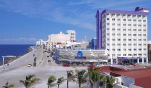 een stadsstraat met gebouwen en palmbomen en de oceaan bij Hotel Lois Veracruz in Veracruz