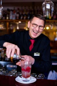 a man in a suit and tie preparing a drink at Landhaus Zu den Rothen Forellen in Ilsenburg