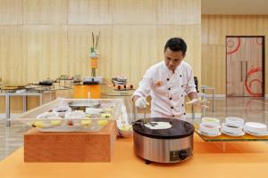 a man standing in a kitchen preparing food at HARRIS Hotel and Conventions Kelapa Gading Jakarta in Jakarta