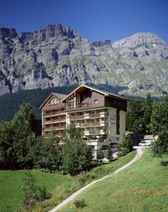 ein Gebäude auf einem Hügel mit einem Berg im Hintergrund in der Unterkunft Alfa Appartements Superior in Leukerbad