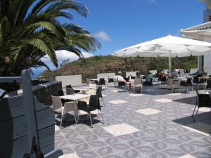 een patio met tafels en stoelen en een parasol bij Hotel Jardim Atlantico in Calheta