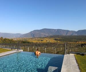 un uomo in una piscina con vista sulle montagne di Hotel Römerrast a Caldaro