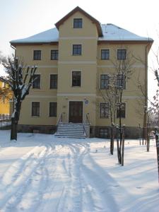 um grande edifício amarelo com neve em frente em Willa Pod Gwiazdami & SPA em Kudowa-Zdrój