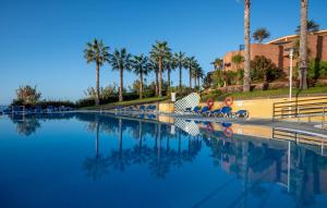 dos personas sentadas en sillas junto a una piscina con palmeras en Monte Mar Palace Hotel, en Ponta Delgada