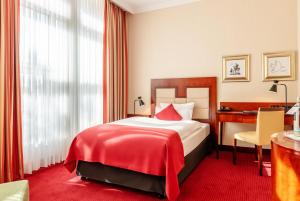 una camera con letto con coperta rossa e scrivania di Amaris Hotel a Bremerhaven