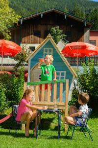 duas crianças sentadas numa mesa em frente a uma casa de brincar em Wohlfühlresort und Feriengut Martinerhof em Sankt Martin am Tennengebirge