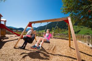 Duas raparigas sentadas num baloiço num parque infantil. em Wohlfühlresort und Feriengut Martinerhof em Sankt Martin am Tennengebirge