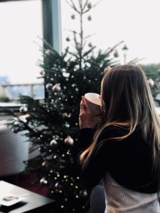 Eine Frau mit einer Kaffeetasse vor einem Weihnachtsbaum in der Unterkunft Hôtel Chalet Royal in Veysonnaz