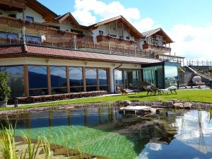 une grande maison avec un étang en face de celle-ci dans l'établissement Hotel Rosslaufhof, à Castelrotto