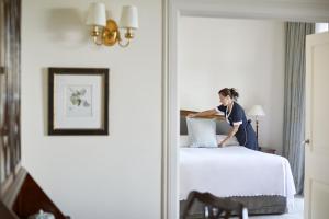 Eine Frau legt Kissen auf ein Bett in einem Hotelzimmer in der Unterkunft Reid's Palace, A Belmond Hotel, Madeira in Funchal