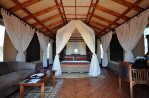 een slaapkamer met een bed met gordijnen en een bank bij Elephant Rock Luxury Camp Tarangire in Kaiti