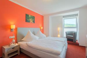 een slaapkamer met een oranje muur met een bed en een stoel bij Hotel Koch Schilt in Irrel