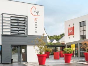 un front de magasin avec des plantes en pot rouge devant lui dans l'établissement ibis Rennes Beaulieu, à Cesson-Sévigné