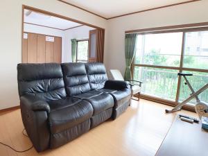 ein Ledersofa im Wohnzimmer mit großem Fenster in der Unterkunft Itsukaichi First Villa Hiroshima in Hiroshima