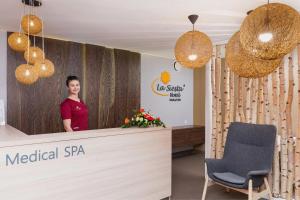 uma mulher em pé em frente a uma recepção de spa médico com uma cadeira em Hotel La Siesta & Medical Spa em Jastrzębia Góra