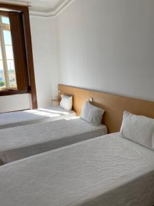 two beds in a room with white sheets and a window at Guesthouse Lusa Atenas in Coimbra