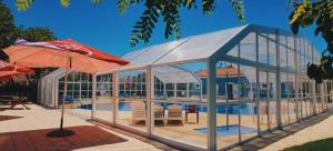 un edificio de cristal con piscina, mesa y sombrilla en Camping Villa Park Zambujeira do Mar, en Zambujeira do Mar