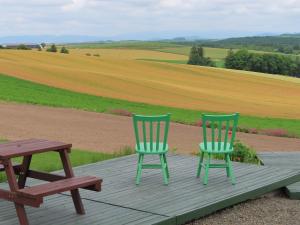 two chairs and a picnic table on a deck with a field at Pension Ken&Mary in Biei