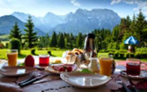 une table avec des assiettes de nourriture et des montagnes en arrière-plan dans l'établissement Bäckeralm© - B&B 16 +, à Mittenwald