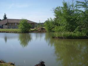 un bacino d’acqua con una casa sullo sfondo di Gites Domaine de la Rochere a Domsure