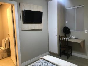 una camera con scrivania e TV appesa a un muro di Piemont Hotel a Curitiba