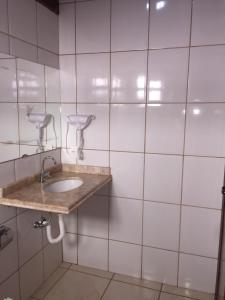 baño con lavabo y pared de azulejos blancos en Pousada Faruk, en Olímpia