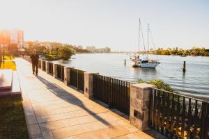 Un uomo che cammina lungo un marciapiede vicino a un fiume con una barca di View Brisbane a Brisbane