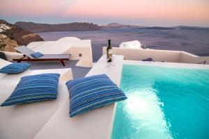 een zwembad aan de zijkant van een huis met blauwe kussens bij Aloia Villas in Oia