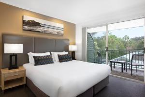 a bedroom with a large white bed and a balcony at BreakFree Aanuka Beach Resort in Coffs Harbour