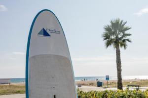 ein Surfbrettschild am Strand neben einer Palme in der Unterkunft Apartamentos Marfina in Castelldefels