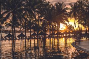 a resort swimming pool with palm trees and a sunset at Mauricia Beachcomber Resort & Spa in Grand Baie