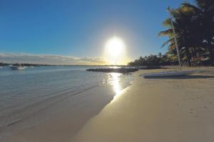 a beach with the sun shining on the water at Mauricia Beachcomber Resort & Spa in Grand Baie