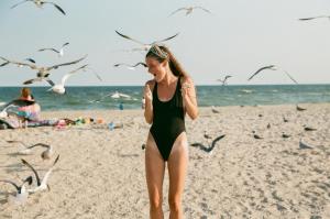 Eine Frau in einem schwarzen Badeanzug am Strand mit Vögeln. in der Unterkunft Piedra Alta Hostel & Suites in La Pedrera