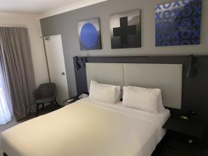 een slaapkamer met een groot wit bed en een stoel bij Silkari Urban CKS Sydney Airport Hotel in Sydney