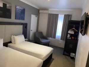 een hotelkamer met 2 bedden en een stoel bij Silkari Urban CKS Sydney Airport Hotel in Sydney