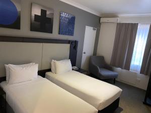 een hotelkamer met 2 bedden en een stoel bij Silkari Urban CKS Sydney Airport Hotel in Sydney