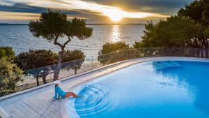 a woman in a blue dress is standing next to a swimming pool at Hotel Pinija in Petrcane