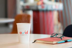 une tasse de café et un ordinateur portable avec un stylo et des verres dans l'établissement avid hotels - Boston Logan Airport - Revere, an IHG Hotel, à Revere